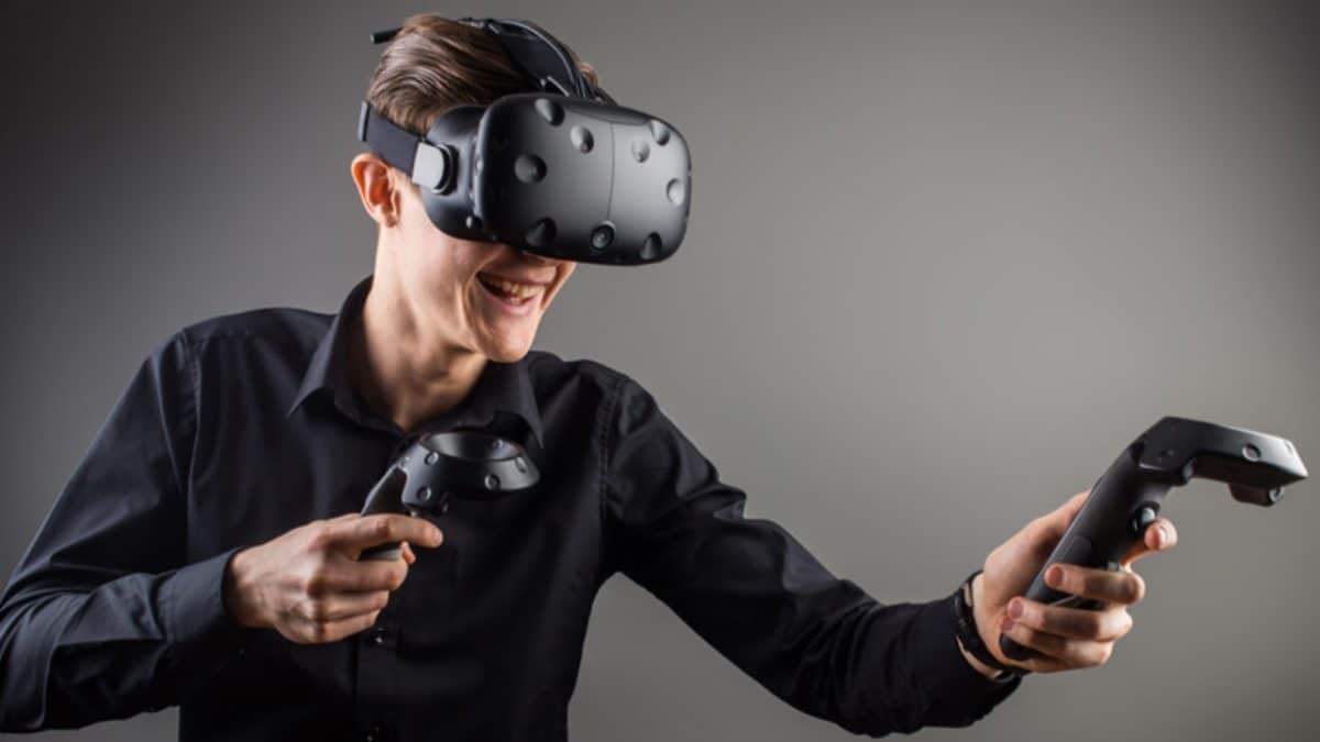 A man stands in front of a gray background wearing a VR headset and controllers.